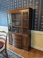 Full view of the Drexel china cabinet showing the upper glass locking hutch, lower drawers, and side cabinets, positioned against floral wallpaper in a dining area.