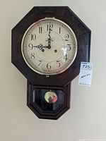 Full view of the Wersch Toll River wall clock showing the octagonal wooden frame, clock face with black numerals and hands, and brass pendulum visible through lower glass panel.