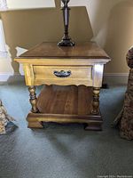Front angled view showing the single drawer with decorative metal handle, turned legs, lower shelf, and wood grain finish.