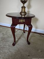 Front view of the oval wooden end table showing single drawer and cabriole legs.