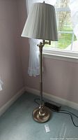 Front view of metal floor lamp with pleated white shade near window