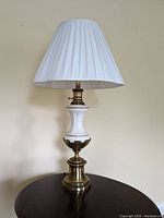 Full view of the white ceramic and brass table lamp with white pleated shade on top