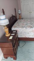 Full view of one night stand next to bed with lamp on top showing overall condition and size.