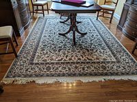 Wide view of the full area rug under a wooden dining table, showing the full pattern and fringe ends on hardwood floors.