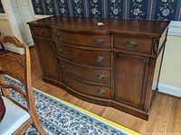 Front view of wooden Drexel server showing curved drawers, brass hardware, side cabinets, with some visible wear and scratches on the veneer.