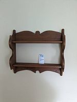 Front view of wooden wall shelf with two shelves showing scalloped sides and decorative top panel.