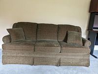 Full front and top view showing the brown plush fabric sofa with attached back cushions and two throw pillows on a carpeted floor.