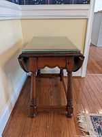 Front view of wooden drop leaf side table with glass protector on top, turned legs visible.