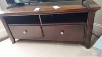 Front view of wooden TV stand showing drawers and open shelves with dark finish and visible wear.