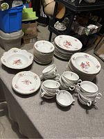 Overview of the full set on a table, showing stacks of plates, bowls, and teacups with floral designs.