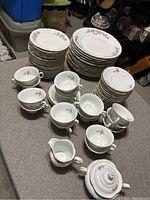 Full set displayed showing plates stacked by size, coffee cups arranged in front, creamer and sugar bowl in front corner. Scene setup in a storage or garage area with visible storage bins and boxes in background.