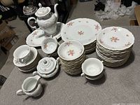 Multiple pieces of floral china dinnerware including plates, cups, sugar bowl, creamer, tea pot and serving platter with floral designs and gold trim.