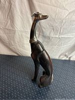 Tall greyhound dog sculpture crafted from wood and silver accents, showing full side view and seated posture.