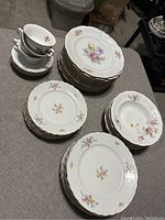 Overview of the collection of white porcelain plates with colorful floral patterns and gold trim, showing variations including dinner plates and bread plates, along with stacked teacups and saucers.