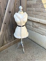 Full view of the mannequin showing white faux fur trim, textured white torso, gray wooden tripod stand, and outdoor setting.