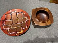 Photograph of both bowls side by side on a grey fabric surface, showing the abstract ceramic bowl and teak wood bowl.