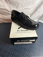 Black patent leather men's tuxedo shoe on top of Dr. Tuxedo by Benjamin Walk Corp. shoebox.