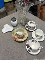 Photo showing all items including the tall cut glass vase, milk glass salt shaker, small milk glass dish, three Royal Albert floral teacups and saucers, and one vintage floral teacup and saucer.