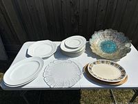 Photo showing all items on a white table including white ceramic plates, clear glass platter, large decorative bowl, and two oval platters.