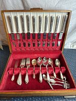 Front view of the WM Rogers stainless silver cutlery set arranged inside the open wooden case showing knives, forks, spoons, and box lining