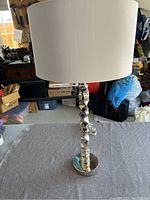 Full view of the silver geometric textured base lamp with white round drum shade on a gray cloth.