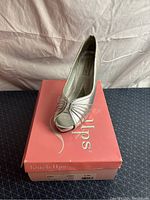 Side and top views of a silver satin satin women's peep toe pump shoe on a pink box labeled Touch Ups.