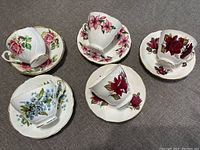 Top down view of five bone china teacup and saucer sets arranged on gray fabric, each with floral decoration in various colors.