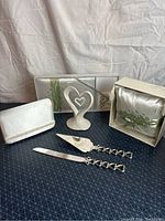 Photo showing the full wedding accessories set including guest book, pen, clutch purse, ceramic heart cake topper, satin ring bearer pillow, and cake serving utensils.