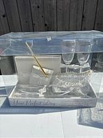 Photo of unopened wedding set packaged in clear plastic box showing toasting glasses, pen, guestbook, garter, and utensils.