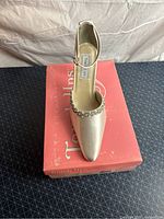 White satin women's pump with rhinestone trim displayed on its pink box labeled Meredith 554M, size 7.5, white, heel height 2.5 inches.