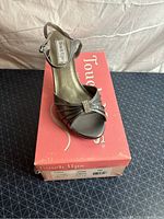 Single gunmetal satin pump resting on pink Touch Ups shoebox showing front view with decorative buckle.