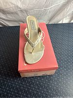 White satin woman's sandal heel on pink Touch Ups shoe box, showing the footbed and thong-style strap.