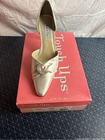 Single women's satin pump on top of original red Touch Ups box with visible logo and wear.