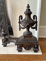 Front view of one andiron showing urn finial, garland swags, pedestal base and scrolled handle
