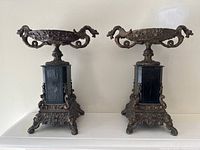 Front view of the pair of antique brass and wood garnitures, showing both pieces side by side on a shelf with visible patina and ornate details.
