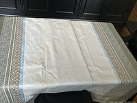 Full view of white tablecloth with intricate jacquard designs and decorative blue and gray border spread on table.