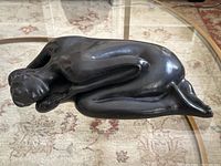 Top and side views showing the overall modernist style and black bronze-like finish of the reclining nude woman sculpture.