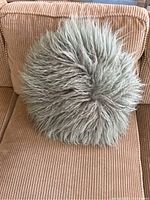 Front full view of the sage green Mongolian lamb decorative pillow on a beige corduroy couch, showing texture and size.