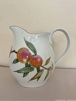 Front and side views of the Royal Worcester water pitcher with the Evesham fruit pattern, showing the curved spout, handle, and decorative fruits and leaves in warm painted colors with gold trim on the rim.
