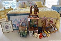 Collection of various figurines, framed prints, small toys, and decor items arranged near a bed.