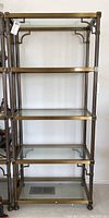 Front view of tall etagere shelving unit showing brass frame and glass shelves.