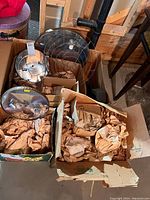 Three cardboard boxes containing chandelier parts: chrome backplates, wire frames and packing paper
