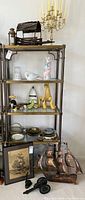 Full view of shelving unit with multiple collectible and decorative items including metal ship, ceramic figurines, miniature cannons, and glassware