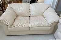 Front view of cream off-white leather loveseat showing cushioned seats and back, visible wear on cushions.