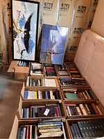 Boxes of books and two framed art prints leaning against wall in basement with insulation visible