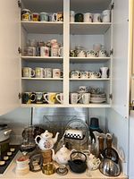 Upper cabinet shelves with various mugs and cups arranged by styles and prints.