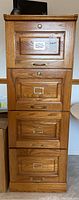 Front view of the oak file cabinet showing four drawers, brass handles and label holders.