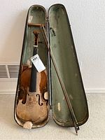 Violin in case with bow, showing violin's front with significant wear and damage, case interior, and bow.