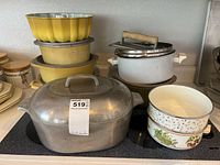 Wide photo of large aluminum roaster with lid alongside stacked enamel bowls showing overall lot condition and arrangement