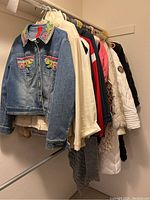 Photo of 7 women's jackets and coats on hangers in a closet, showing variety of fabrics and colors including denim, light beige leather, and white quilted coat.